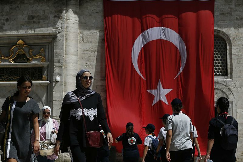 People walk recently in Istanbul past a Turkish flag draping a mosque. Treasury and Finance Minister Berat Albayrak sought to calm investors’ jitters Thursday. 
