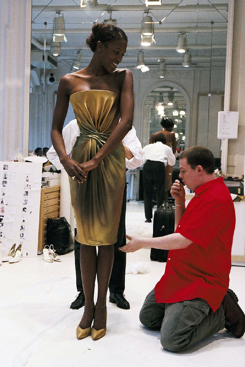 Circa 1992, a young Lee Alexander McQueen adjusts the hem of a dress of an unidentified model in this still from the bio-doc McQueen. 