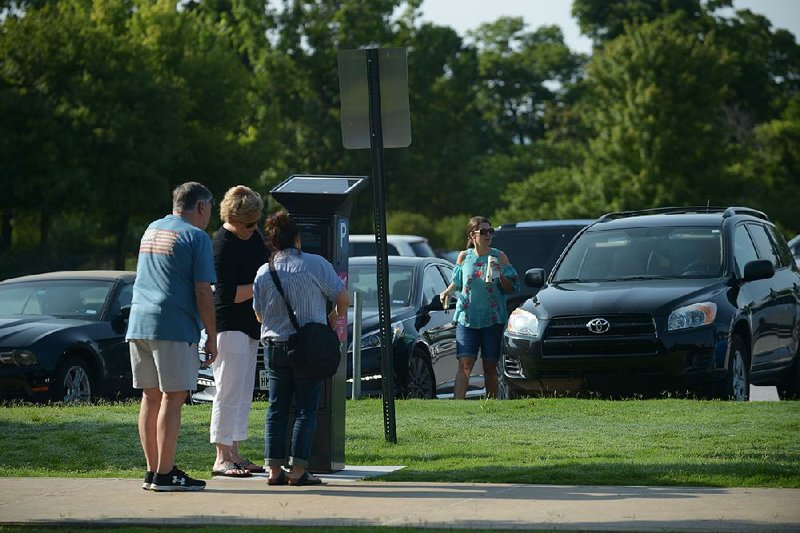 Visitors read instructions Saturday on a paid-parking kiosk for Lot 71 on the University of Arkansas, Fayetteville campus. UA’s plans for a new high-tech parking management system have been delayed. 