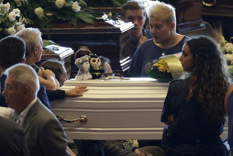 People stand by a small white coffin of a child ahead of a funeral service for some of the victims of a collapsed highway bridge, in Genoa's exhibition center Fiera di Genova, Italy, Saturday, Aug. 18, 2018. Saturday has been declared a national day of mourning in Italy and includes a state funeral at the industrial port city's fair grounds for those who plunged to their deaths as the 45-meter (150-foot) tall Morandi Bridge gave way Tuesday. (AP Photo/Gregorio Borgia)