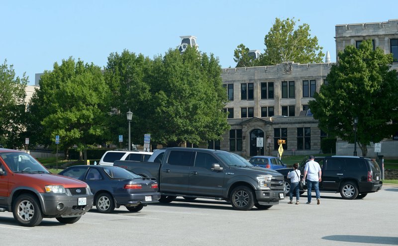 NWA Democrat-Gazette/ANDY SHUPE Visitors walk from their cars Saturday after parking in Lot 71 on the University of Arkansas campus in Fayetteville. The University of Arkansas, Fayetteville announced plans a year ago to begin using car-mounted cameras to enforce parking regulations, but the system has not been installed despite records showing nearly $300,000 made in payments to NuPark.