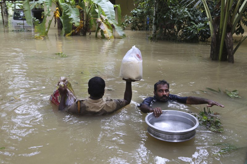 An Indian policeman, left, and a volunteer carry essential supplies for stranded people in a flooded area in Chengannur in the southern state of Kerala, India, Sunday, Aug.19, 2018. Some 800,000 people have been displaced and over 350 have died in the worst flooding in a century. (AP Photo/Aijaz Rahi)