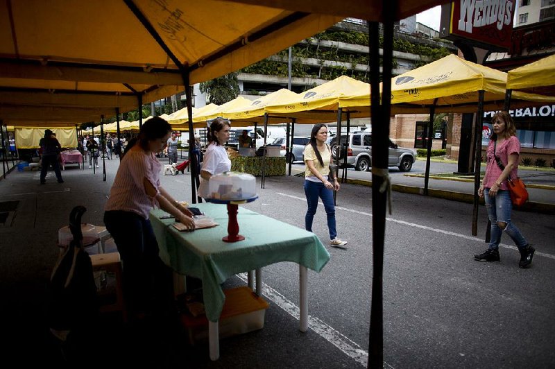 People walk past empty sales stands at a street market in Caracas, Venezuela, on Saturday. Venezuela launched a series of economic-overhaul measures on Monday, beginning with the release of a currency with five fewer zeros in a bid to tame soaring inflation. 