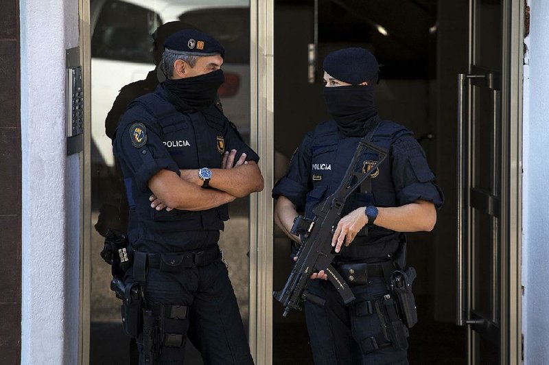 Catalan police officers stand guard at the entrance of a building near Barcelona, Spain, during a raid Monday. Police said they shot a man who attacked officers with a knife at a police station. 