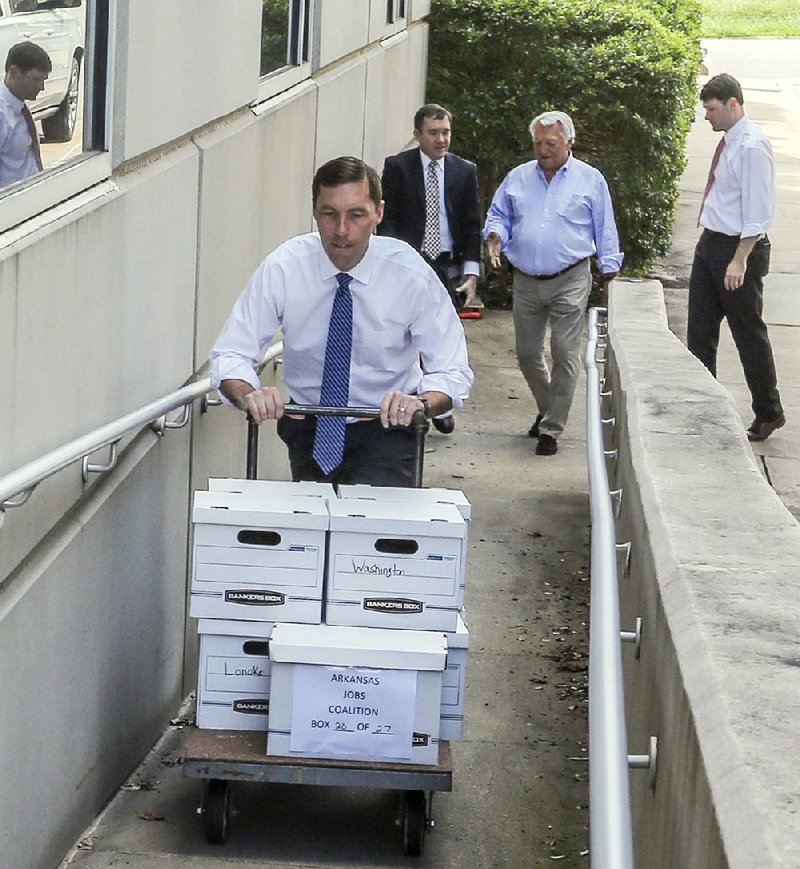 Nate Steel, legal counsel for Driving Arkansas Forward, a coalition supporting a ballot measure to expand casino gambling in Arkansas, pushes a cart full of signed petitions Tuesday at the state Capitol, as Aaron Sadler and Don Tilton follow. Sadler (left) is a spokesman for the group, and Tilton is chairman of the Driving Arkansas Forward committee. 