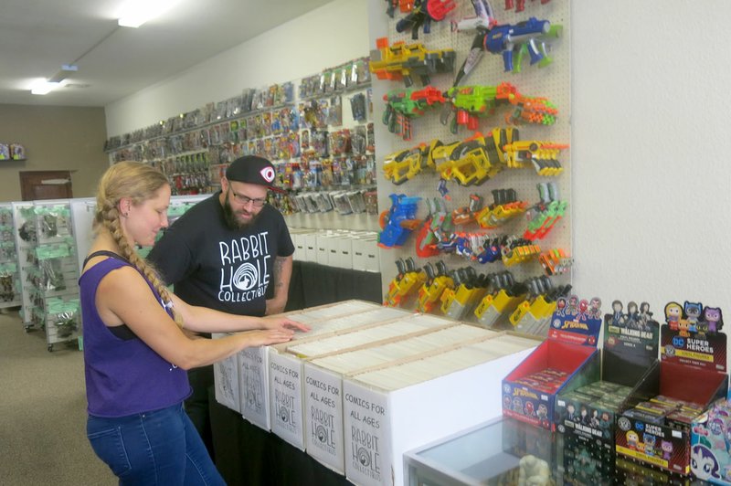 Westside Eagle Observer/SUSAN HOLLAND Rachel and Edward Wilson look over a few of the items in their vast selection of comic books at Rabbit Hole Collectibles, 107 Main Street S.E., in Gravette. Displays on the walls and shelves offer many toys and games. Books, movies, records and CDs are also available at the shop which opened August 1.