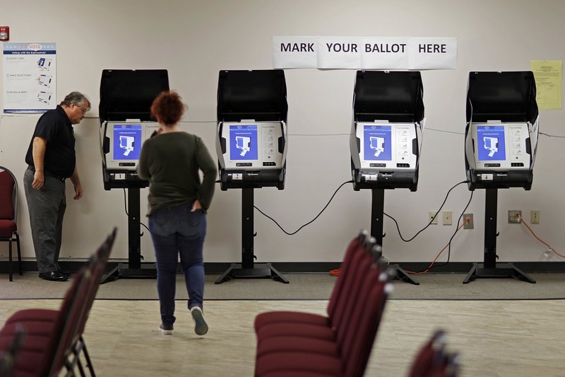  In this Thursday, Oct. 19, 2017, file photo, Kelly Monroe, investigator with the Georgia Secretary of State office, left, takes a look at a new voting machine that produces a paper record being tested at a polling site in Conyers, Ga. 