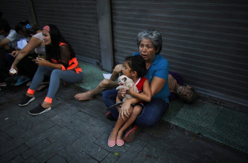 Maryeli Verde holds her niece Yalin, who clutches her cat Will, as Yalin's grandfather Tonisio, who is sick, lies behind them after they evacuated their apartment on the ninth floor after a powerful earthquake shook eastern Venezuela on Tuesday, Aug. 21, 2018. 