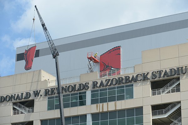 Workers with Multi-Craft Contractors and Sign Studio work to guide a panel of a large Razorback mascot logo Thursday, Aug. 9, 2018, onto the south side of Razorback Stadium in Fayetteville. 