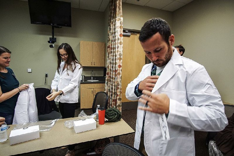 First-year medical student John Wilson tries on his white coat earlier this month while on a break during orientation week for freshmen at the University of Arkansas for Medical Sciences College of Medicine. More photos are available at arkansasonline.com/826uams.