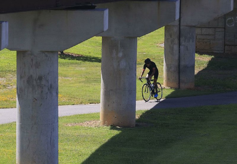 A cyclist passes under the Big Dam Bridge as he rides the Arkansas River Trail in Little Rock in this 2018 file photo. 