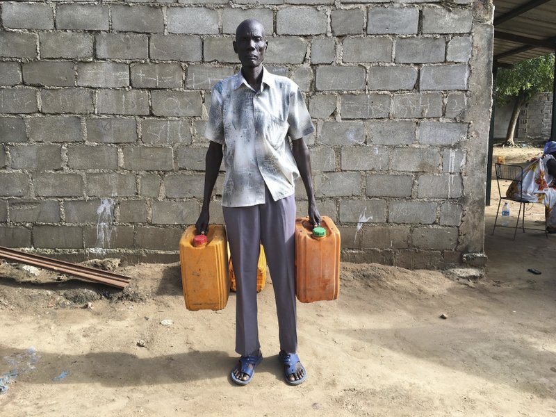 FILE - In this Monday, Oct. 2, 2017 file photo, black market fuel trader Nyuol Deng holds empty jerrycans outside his house in Juba, South Sudan. Emboldened by a new peace deal, civil war-torn South Sudan says it will resume oil production in a key region in September 2018 to make up for more than $4 billion of revenue lost during years of fighting. (AP Photo/Sam Mednick, File)