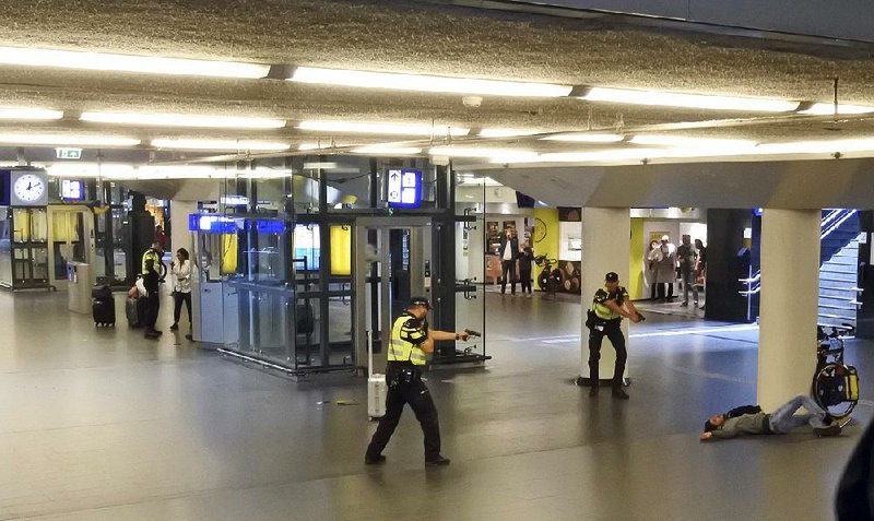 Dutch police officers keep their guns aimed at a man suspect- ed in the Friday stabbings of two people at a railway station in Amsterdam. Officers shot and wounded the man, who remained hospitalized Saturday. 