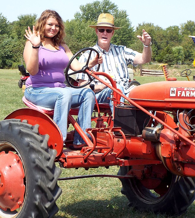 Westside Eagle Observer/RANDY MOLL Makayla Henson, a student at Rogers Heritage High School, takes a tractor-driving lesson from Glenn Smith, member of the Tired Iron of the Ozarks, and drove with him in the noon Parade of Power on one of his dual-seat and dual-control Farmall tractors during the opening day of the fall show of the Tired Iron club on Sept. 8, 2017. This year's fall show begins on Friday.