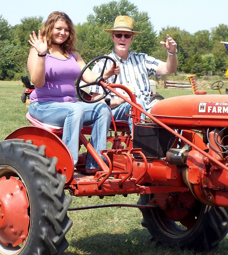 Westside Eagle Observer/RANDY MOLL Makayla Henson, a student at Rogers Heritage High School, takes a tractor-driving lesson from Glenn Smith, member of the Tired Iron of the Ozarks, and drove with him in the noon Parade of Power on one of his dual-seat and dual-control Farmall tractors during the opening day of the fall show of the Tired Iron club on Sept. 8, 2017. This year's fall show begins on Friday.
