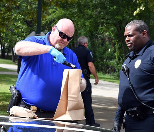 The Sentinel-Record/Grace Brown RECOVERED WEAPON: Hot Springs police Cpl. Patrick Langley, right, looks on as Detective Sean Stillian places a gun reportedly found inside a vehicle that was allegedly involved in a shooting into an evidence bag in the 100 block of Orange Street Thursday.