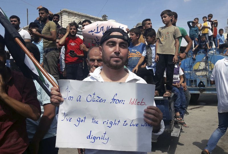 This image courtesy of Mustafa Alabdullah, an activist and resident of Idlib, shows a protester holding a placard, in Harim, a town in Idlib province, Syria, Friday, Sept 7, 2018. The rallies were part of a day of protests against Syrian President Bashar Assad and his troops' imminent offensive against Idlib, the last bastion of rebels in Syria. The Friday rallies came as Presidents of Iran, Turkey and Russia are meeting in Tehran to discuss the war in Syria. The summit may determine whether diplomacy halts any military action in Idlib and its surrounding areas, home to more than 3 million people. Nearly half of the area's residents are already displaced from other parts of Syria and have refused to reconcile with the Syrian government. (Courtesy of Mustafa Alabdullah via AP)