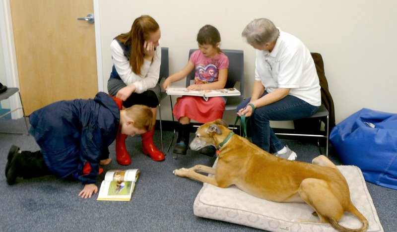 Photo submitted Dusty, a certified therapy dog, listened as a family read to him in the Siloam Springs Public Library. Dusty and his owner Memerley McElheny visit the library twice a month so that children of all ages can have a chance to read to him.