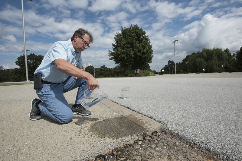 NWA Democrat-Gazette/J.T. WAMPLER Bill HagenBurger, Beaver Water District plant engineer, pours water Thursday to demonstrate how water seeps through the district's pervious surface of their green parking lot in Lowell. Green parking lots help mitigate pollution in stormwater, reduce flooding and cut down on the amount of heat off of hard surfaces, according to the National Parking Association.