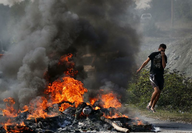A Kosovo Albanian runs past a fire burning at a roadblock Sunday in Vojtesh, Kosovo.