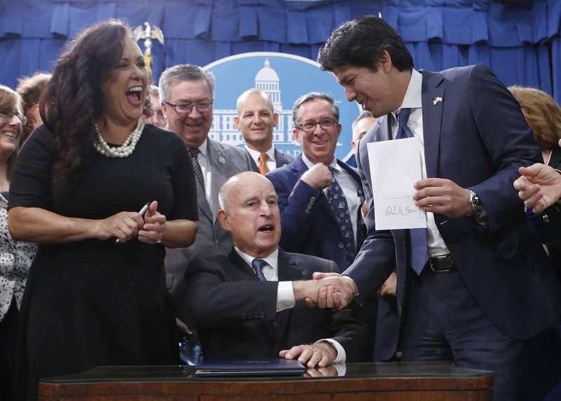 State Sen. Kevin de Leon, D-Los Angeles, right, shakes hands with Gov. Jerry Brown after Brown signed his environmental measure SB100, Monday, Sept. 10, 2018, in Sacramento, Calif. SB100 sets a goal of phasing out all fossil fuels from the state's electricity sector by 2045. Assemblywoman Lorena Gonzalez Fletcher, D-San Diego, left, who carried the bill in the Assembly, reacts. (AP Photo/Rich Pedroncelli)