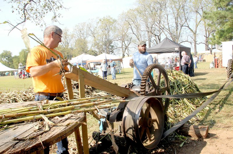 FILE PHOTO Visitors to the annual Cane Hill Harvest Festival can use how sorghum molasses is made. In this photo from the 2017 Festival, Earl Rowe of Lincoln, left, and Luke Haegele of Cane Hill use a crushing mill powered by tractor to get the juice from sorghum grass, grown specifically for the Cane Hill Harvest Festival each year.