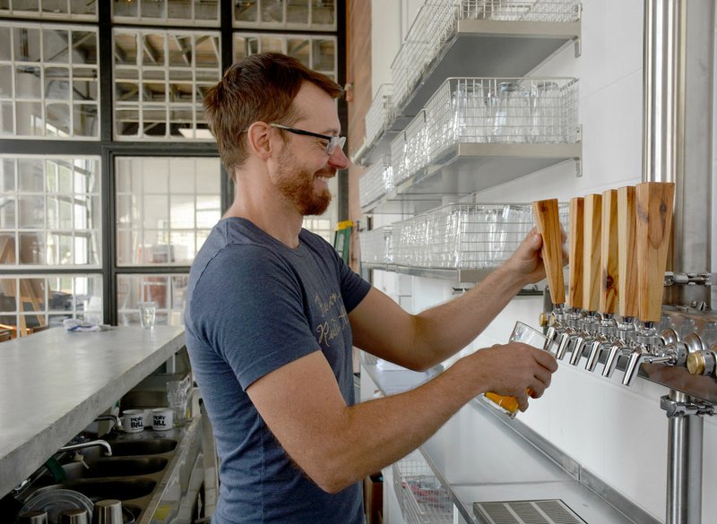 Janelle Jessen/Herald-Leader Casey Letellier poured freshly brewed beer from the tap in Ivory Bill Brewing. The tap handles are made from reclaimed cypress shelving from Siloam Springs' original 1940s IGA Grocery Store building.