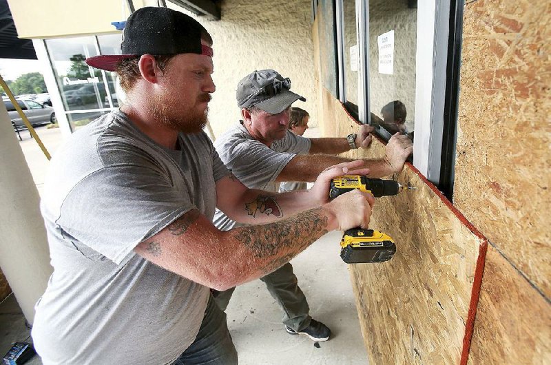 Dominic Carucci (from left), Michael Waldo and Robert McKeehan attach sheets of plywood to the front of a dress store Wednesday in Rocky Mount, N.C., about 100 miles inland. 