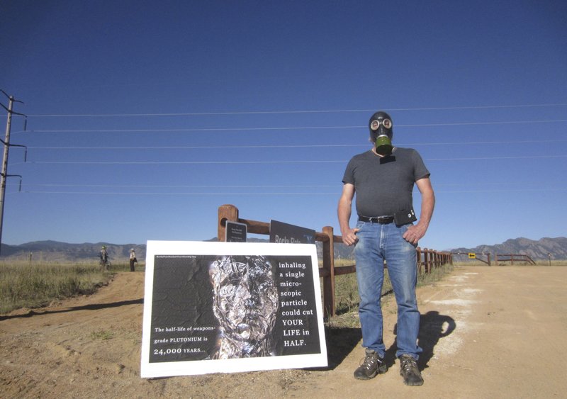 Stephen Parlato wears a gas mask next to his sign warning about the dangers of plutonium at Rocky Flats National Wildlife Refuge outside Denver on Saturday, Sept. 15, 2018, the first day the refuge was open to the public. The refuge is on the outskirts of a former U.S. government factory that manufactured plutonium triggers for nuclear weapons. (AP Photo/Dan Elliott)