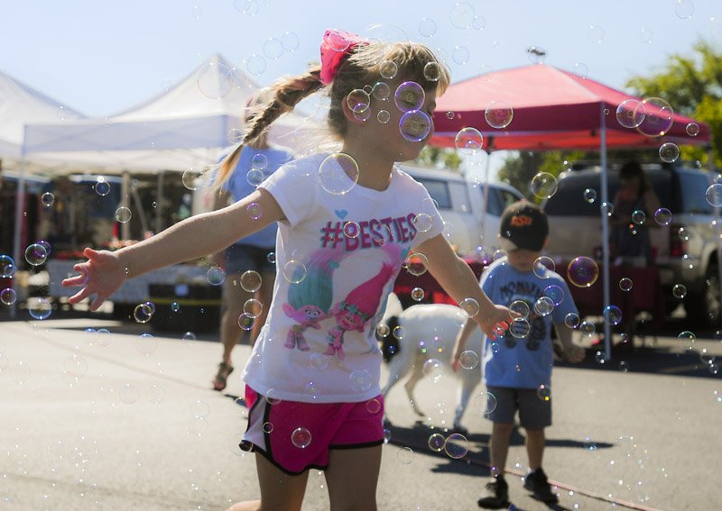 NWA Democrat-Gazette/CHARLIE KAIJO Natalli Putnam, 5, of Bella Vista runs through bubbles at the Bella Vista farmer's market, Sunday at Sugar Creek Center. Police and fire department personnel were at the Bella Vista Farmers Market shaking hands and showing their trucks and equipment off to the visitors while they shopped for fresh produce and handmade goods. The Bella Vista Farmers Market operates every Sunday through October 14 from 9 a.m. to 2 p.m. in the parking lot of Sugar Creek Center. Fresh produce and locally handmade goods are available.