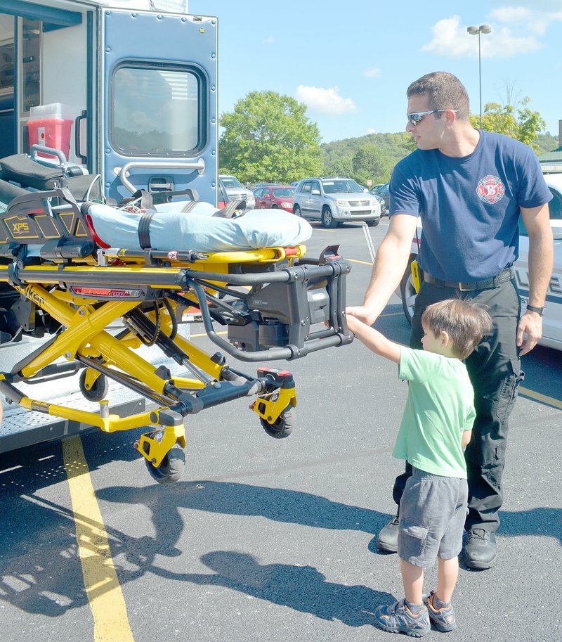 Keith Bryant/The Weekly Vista Bella Vista firefighter-paramedic Alex Cutbirth shows 3-year-old P.J. Caniglia how to raise and lower a powered stretcher. Cutbirth said this is a great chance to let kids take a close look at fire and EMS equipment.