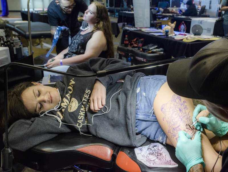 Artist “Tex” (right) works Friday on a tattoo for Tyler Armstrong of Los Angeles during the Ink & Art in the Ozarks tattoo show at the town square in Fayetteville. The event included live tattooing, local artists and celebrity talent and performances. The event continues today.