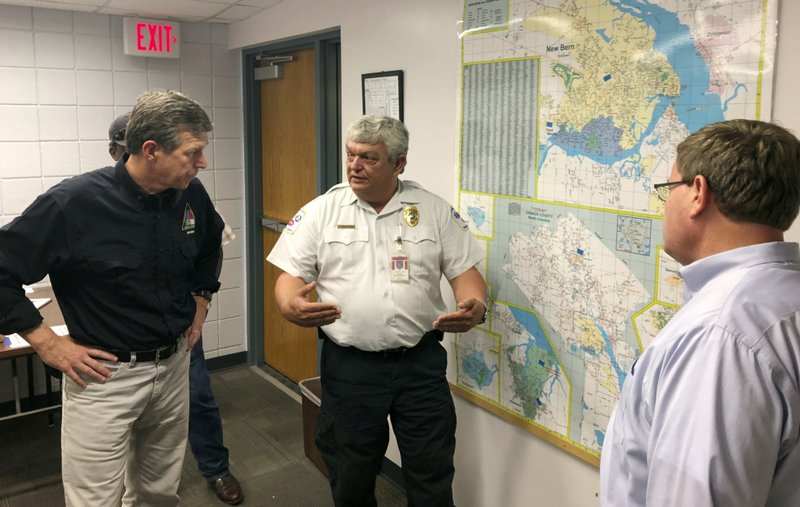 In this Sept. 17, 2018 photo, Craven County Emergency Services Director Stanley Kite, center, discusses flooding and damage caused by Hurricane Florence with North Carolina Democratic Gov. Roy Cooper, left, and Republican state House Speaker Tim Moore, right, in New Bern, N.C.  (AP Photo/Gary D. Robertson)