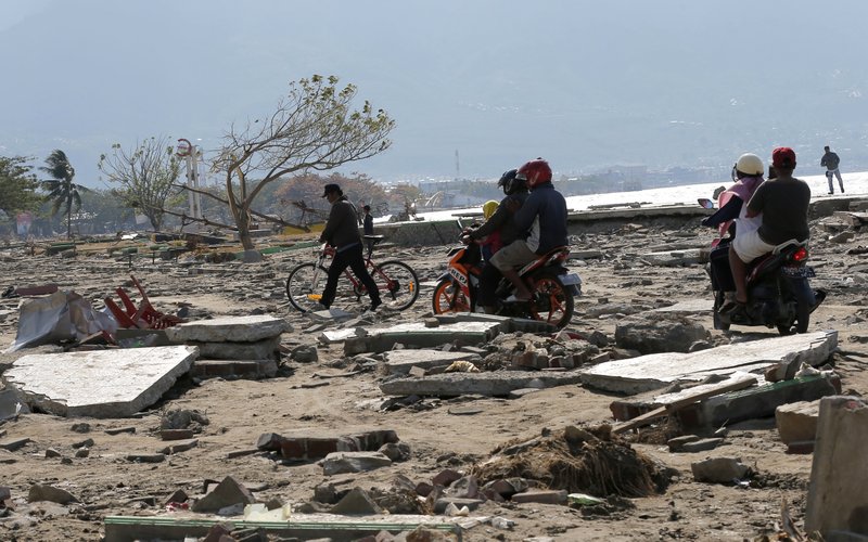 People move through rubble and debris following a massive earthquake and tsunami at Talise beach in Palu, Central Sulawesi, Indonesia, Monday, Oct. 1, 2018. A mass burial of earthquake and tsunami victims was being prepared in a hard-hit city Monday as the need for heavy equipment to dig for survivors of the disaster that struck a central Indonesian island three days ago grows desperate. (AP Photo/Tatan Syuflana)