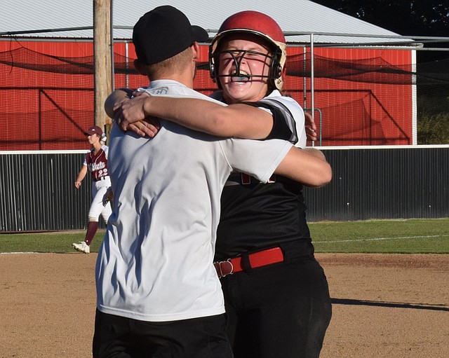 RICK PECK/SPECIAL TO MCDONALD COUNTY PRESS McDonald County's Kylie Helm celebrates with assistant coach Kyle Smith after knocking in the winning run in the Lady Mustangs' 3-2 win over Logan-Rogersville on Sept. 27 at MCHS.