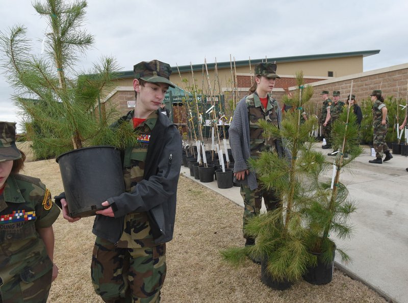 NWA Democrat-Gazette/FLIP PUTTHOFF Jake Provenza (left) with the Young Marines youth organization carries a free tree for a customer on April 14 during the Bentonville's tree giveaway at the Bentonville Community Center. The event distributed 400 trees of several varieties to city residents.