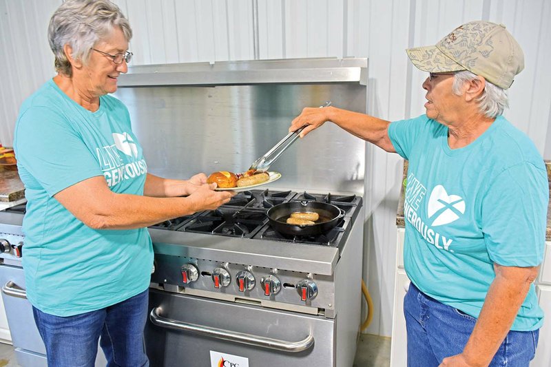 Eunice LaMar, left, and her sister Ann Hogrefe prepare a sample plate of homemade bratwursts, similar to what will be served at the Augsburg Fall Festival on Saturday. Their father, the late Elmer Hogrefe, and brother, Eddie Hogrefe, were the contractors for the current church building, which was dedicated on March 9, 1980.