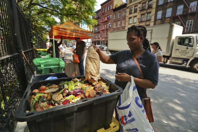 In this Aug. 29, 2018, photo, Sabrina Deshong dumps leftovers from her lunch into a compost collection point operated by GrowNYC in New York. (AP Photo/Stephen Groves)
