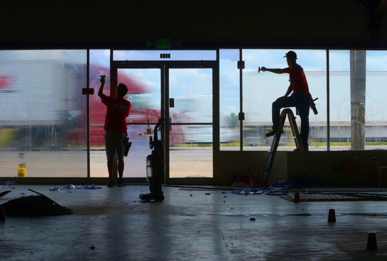 NWA Democrat-Gazette/ANDY SHUPE Stephen Medley (left) and Steven Boak, both window cleaners with Fish Window Cleaning in Springdale, work together Tuesday with Josh Carson (not picture) to remove window tinting from the front windows in the former Markets Unlimited building at 5148 N. Thompson St. in Bethel Heights. The building is expected to be home for Fence Co., a fencing company based in Springdale.
