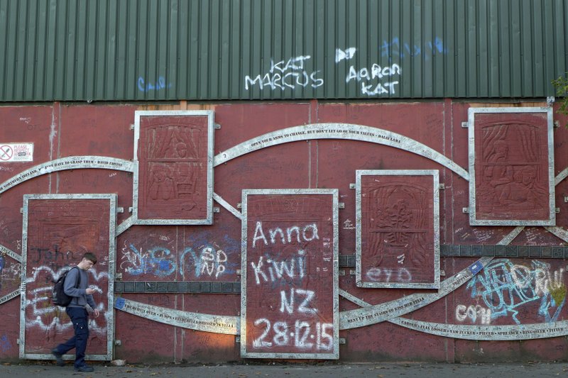 In this photo taken on Wednesday, Oct. 10, 2018, a man walk past a section of one of the Northern Ireland &quot;peace walls&quot; in Cupar Way, Belfast, Ireland. The land around the small town of Carrickcarnan, Ireland is the kind of place where Britain&#x2019;s plan to leave the European Union walks right into a wall - an invisible one that is proving insanely difficult to overcome. Somehow, a border of sorts will have to be drawn between Northern Ireland, which is part of the United Kingdom, and EU member country Ireland to allow customs control over goods, produce and livestock once the U.K. has left the bloc. (AP Photo/Lorne Cook)