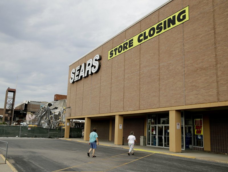 In this July 8, 2017, file photo people walk into a Sears store slated for closing that is next to a mall that is being torn down in Overland Park, Kan. Sears has filed for Chapter 11 bankruptcy protection Monday, Oct. 15, 2018, buckling under its massive debt load and staggering losses. The company once dominated the American landscape, but whether a smaller Sears can be viable remains in question. (AP Photo/Charlie Riedel, File)