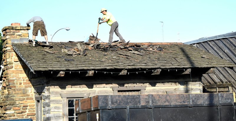 Westside Eagle Observer/MIKE ECKELS A roofing company removes old rotten wood shingles from the log cabin in downtown Decatur Oct. 3. The historic structure has been in need of a new roof for many years. A new cedar-shingle roof was put in place by late afternoon.