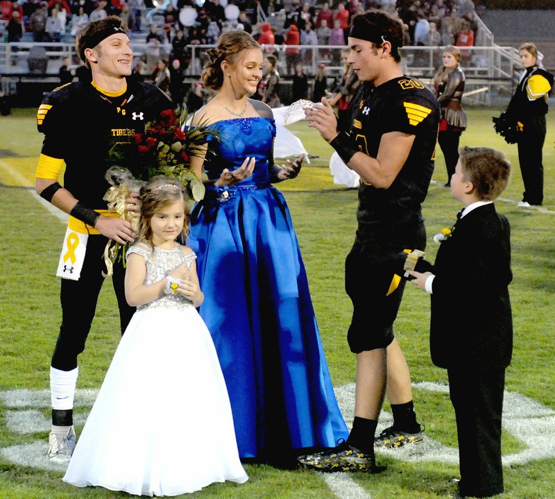 MARK HUMPHREY ENTERPRISE-LEADER Prairie Grove captain Garrett Heltemes displays reverence for the Homcoming Queen crown he handles delicately while about to crown 2018 Prairie Grove High School Homecoming queen Raegan Rochier. Co-captain Hyler Kaine Caswell (right) served as Rochier's other escort with attendants Lottie Pinkley and Finn Foster also participating in the ceremony.