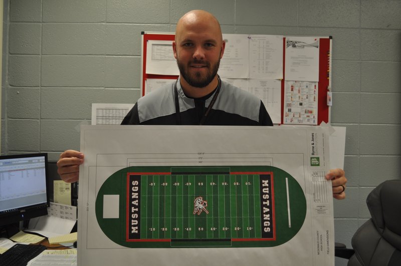 RACHEL DICKERSON/MCDONALD COUNTY PRESS McDonald County High School athletic director Bo Bergen holds a mock-up of the new turf field that will be installed. Along with a new athletic sports complex, the field is part of improvements to the school's athletics program.