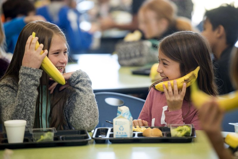NWA Democrat-Gazette/BEN GOFF @NWABENGOFF Alison Tennyson (left) and Aubrey Standard, both 4th graders, pretend their bananas are telephones Wednesday during lunch at Janie Darr Elementary School in Rogers. Rogers Public Schools administrators visited the school for lunch as part of the district's recognition of National School Lunch Week. The district's schools serve 11,000 meals each day, according to Ashley Siwiec, communications director for the district.