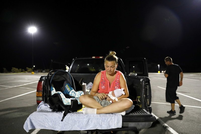 In this Monday, Oct. 15, 2018 file photo, Lorrainda Smith sits with her 2-day-old son, Luke, as she contemplates with her husband, Wilmer Capps, right, sleeping in their truck in a parking lot after their home was damaged from Hurricane Michael and they were told a nearby shelter was closed, in Panama City, Fla. Wilmer Capps says he and wife Lorrainda Smith had no choice but to camp out at the store the night their son Luke was released from an Alabama hospital because their home in Panama City, Florida, was badly damaged by the storm. (AP Photo/David Goldman, File)

