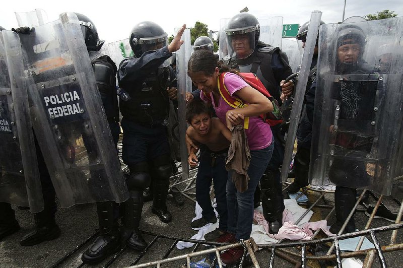 A Honduran migrant mother and child cower Friday as they are surrounded by Mexican federal police in riot gear at the border crossing in Ciudad Hidalgo, Mexico. 