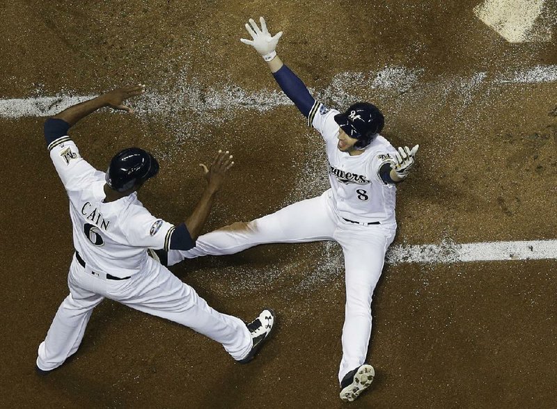 Milwaukee’s Lorenzo Cain (left) congratulates Ryan Braun after scoring on a first-inning hit by Jesus Aguilar in the first inning of Game 6 of the National League Championship Series on Friday night.