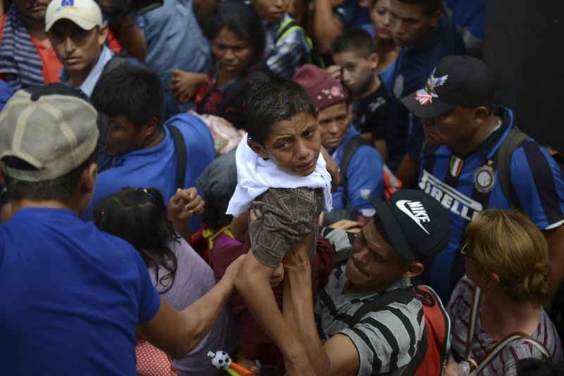 A boy cries as he is brought back down after an unsuccessful attempt to lift him over a border fence, in Tecun Uman, Guatemala, Friday, Oct. 19, 2018. Earlier in the day, waving Honduran flags and carrying umbrellas to protect against the sun, thousands of migrants arrived at the Guatemalan side of the border with Mexico, demanding they be allowed passage. (AP Photo/Oliver de Ros)