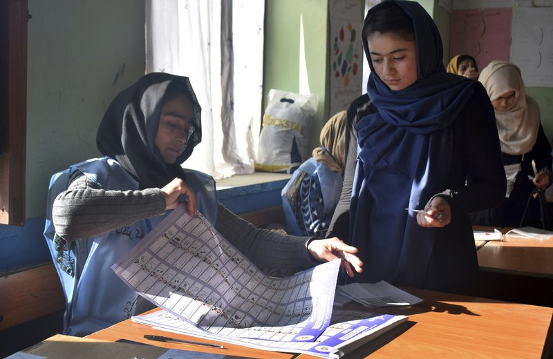 In this Saturday, Oct. 20, 2018, photo, an employee of Independent Elections Commission, left, prepares a ballot paper for a young female voter before casting her vote at a polling station in Faizabad, center of northern Badakhshan province, Afghanistan&#x2019;s parliamentary elections entered a second day on Sunday, Oct. 21, 2018, following violence and chaos that caused delays and interruptions on the first day of polling. (AP Photo/Omer Abrar)